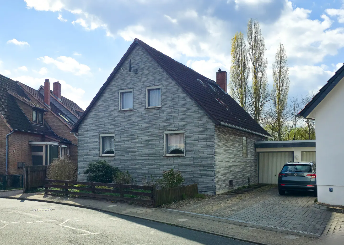 A two-story gray stone house with a brown roof, a garage, and a car parked in the driveway.