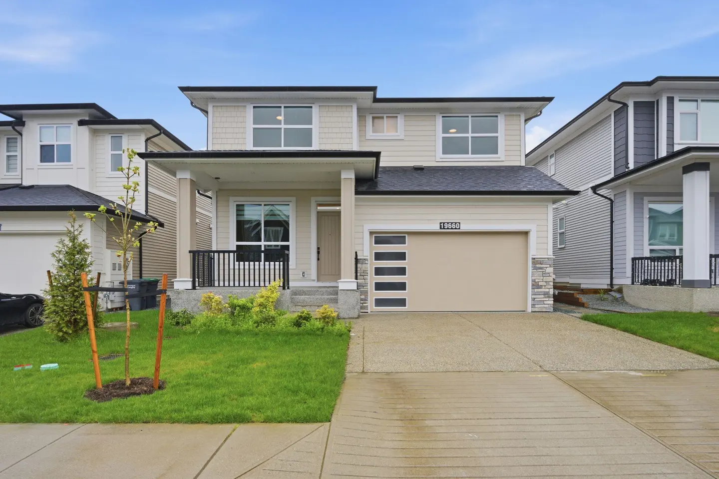 Beige two-story house with a black roof, a beige garage door with windows, and a green lawn.