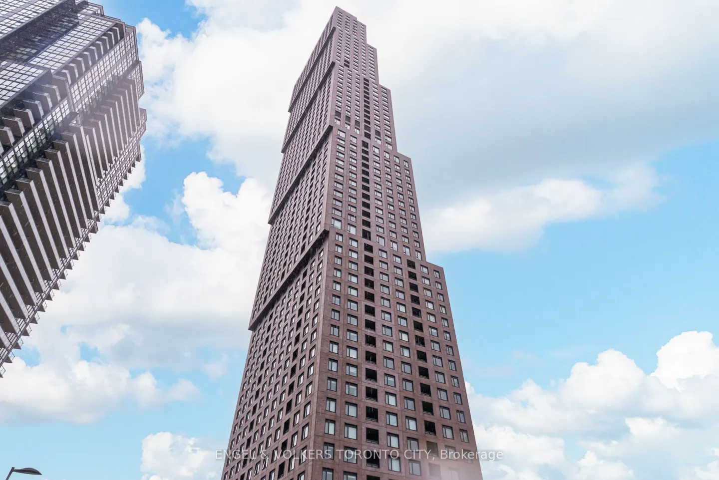 A low-angle shot of a tall, brown skyscraper with many windows against a blue sky with white clouds.