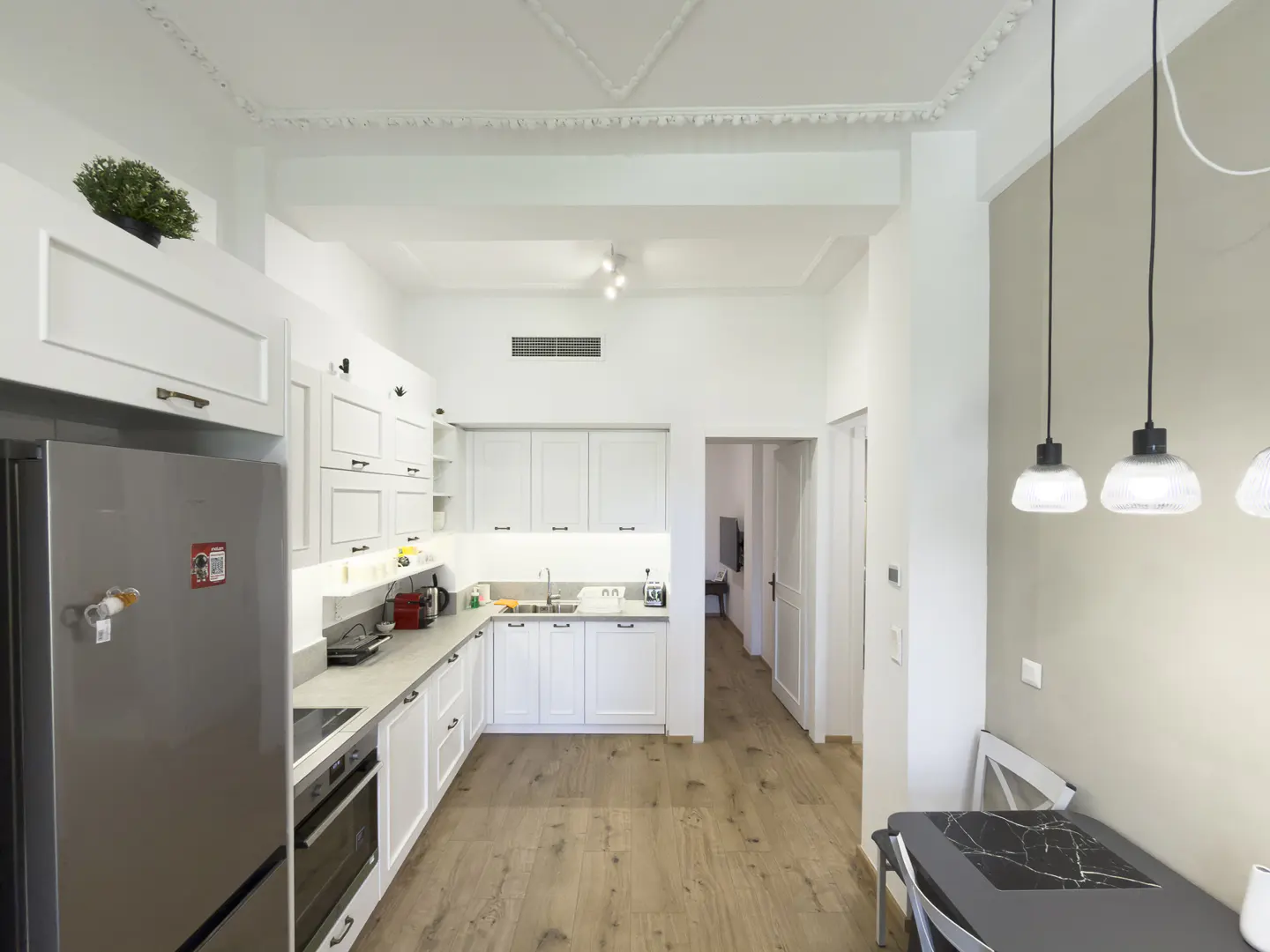 Bright, modern kitchen with white cabinets, stainless steel appliances, and wood floors. Pendant lights hang over a gray table.