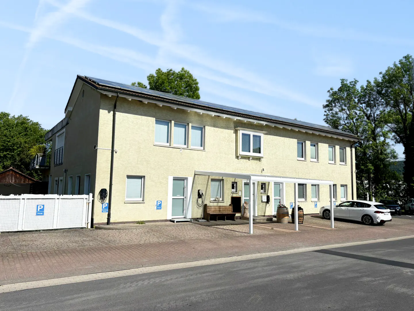 Two-story beige building with solar panels on the roof. A white car is parked in front of the building.