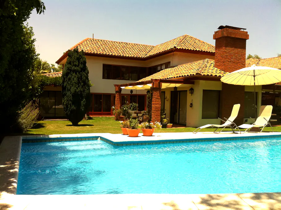Backyard view of a two-story house with a red tile roof, a pool, and lounge chairs.