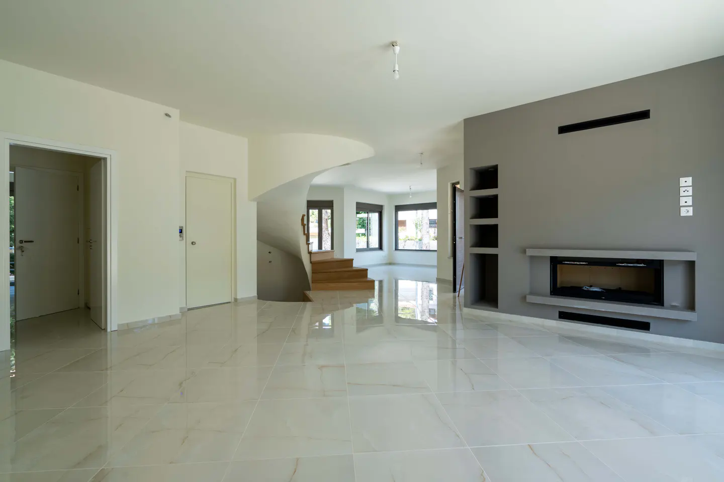 Modern living room with white marble floors, a grey accent wall featuring a fireplace, and a curved wooden staircase.