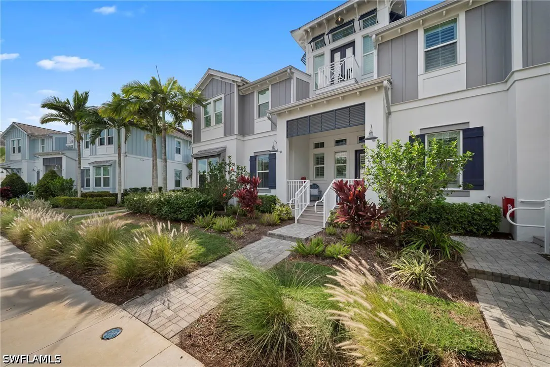 Row of two-story townhouses with white and gray exteriors, blue shutters, and lush landscaping under a blue sky.