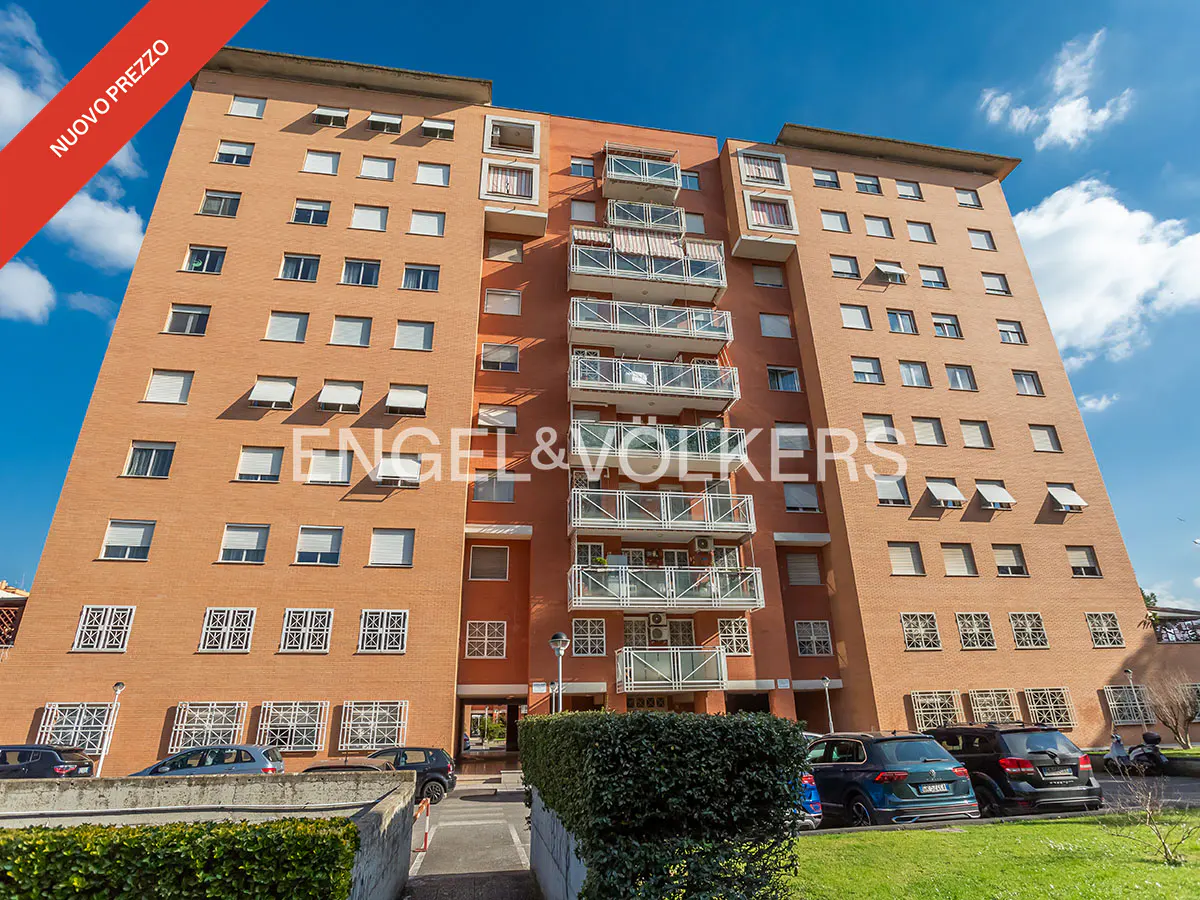 Exterior view of a tall, brick apartment building with white balconies and windows under a blue sky. "Engel & Völkers" logo is visible.