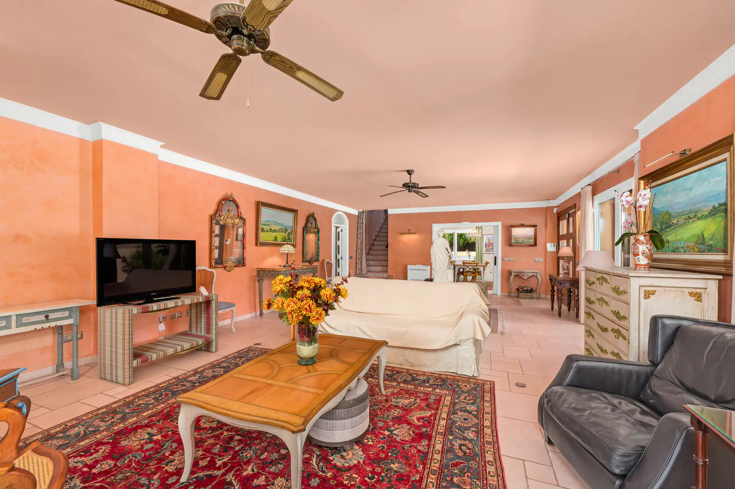 Spacious living room with peach walls, a red patterned rug, a wooden coffee table, and a black leather armchair.
