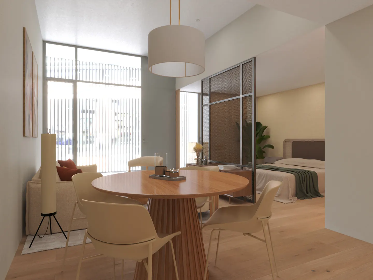 Modern studio apartment with a round wooden dining table, cream chairs, and a bedroom area separated by a metal screen.