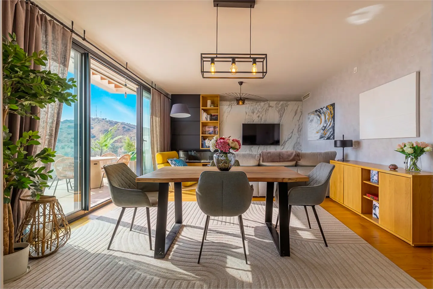 Bright living room with a wood table, gray chairs, and a view of mountains through sliding glass doors.