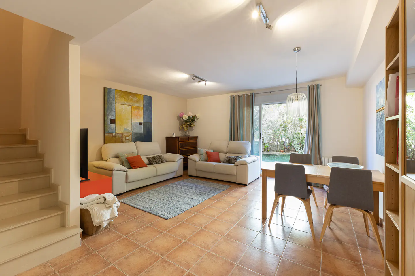 Living room with tile floor, two sofas, a dining table with four chairs, and a sliding glass door to a garden.