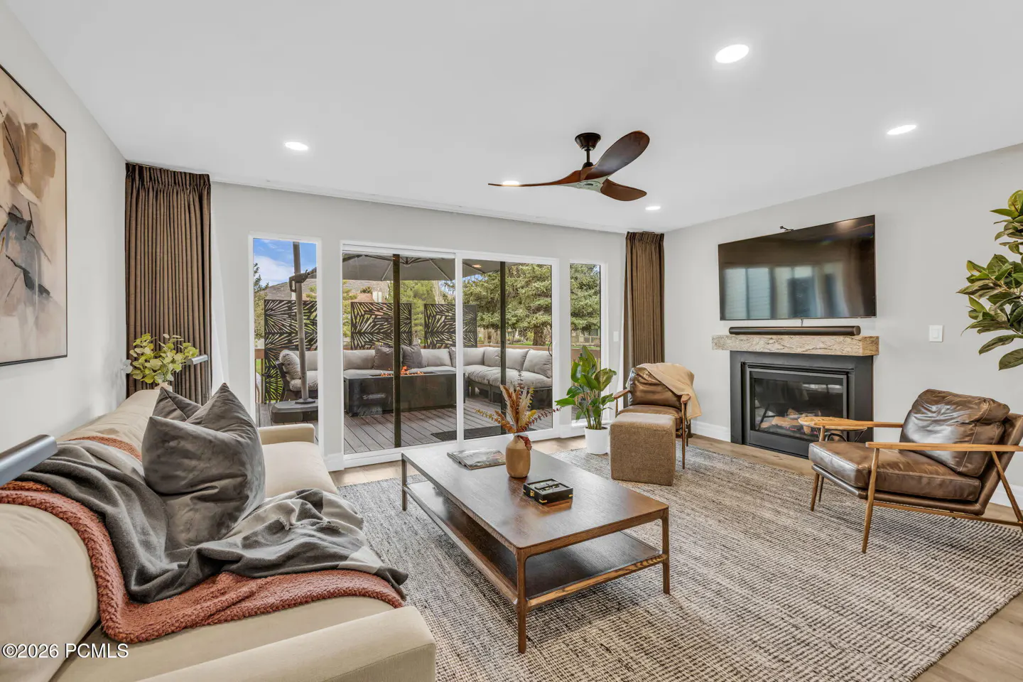 Living room with a beige sofa, brown leather chairs, a fireplace, and a sliding glass door to a patio.