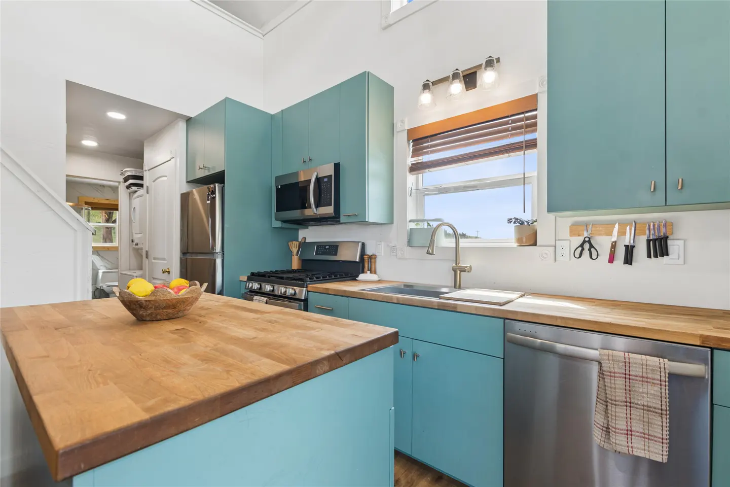 Bright kitchen with light blue cabinets, butcher block countertops, and stainless steel appliances. A wooden bowl of fruit sits on the island.