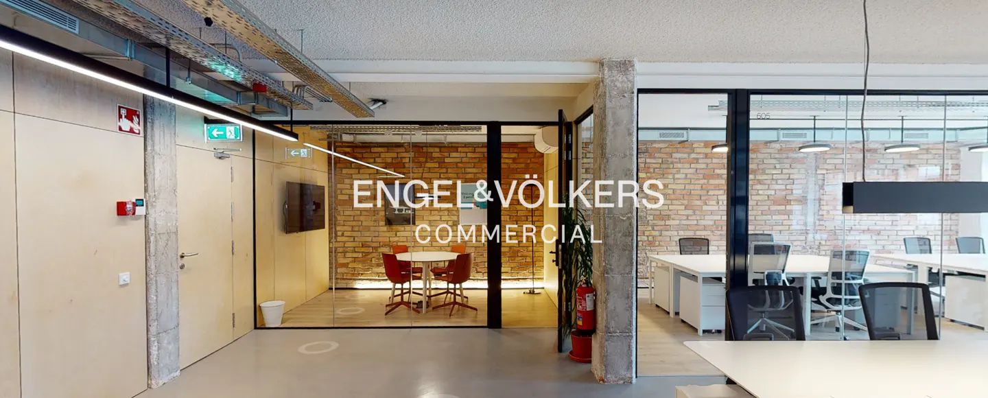 Office interior with glass-walled rooms, brick walls, and modern desks. "Engel & Völkers Commercial" is displayed on the glass.