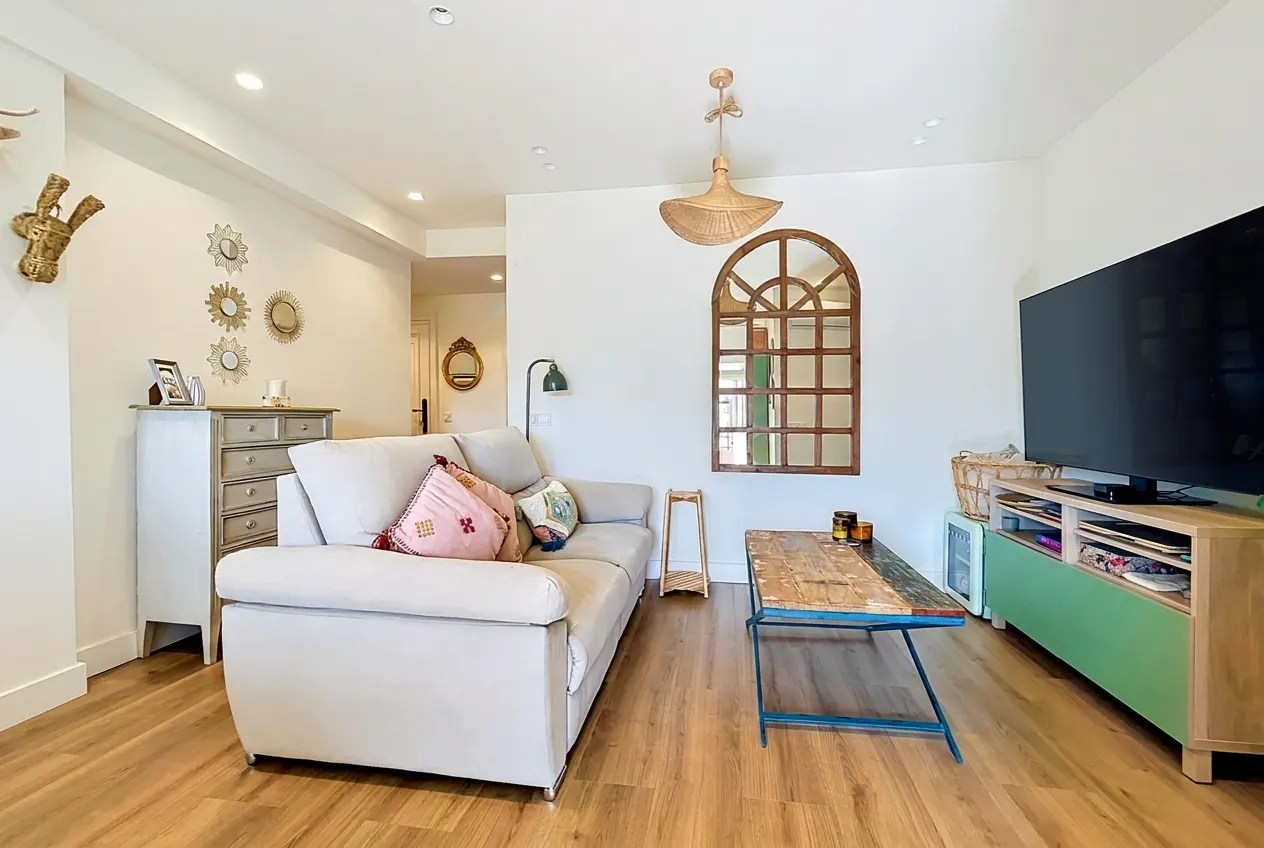Bright living room with a beige sofa, rustic wooden coffee table, large TV, and decorative wall mirrors on wood floors.