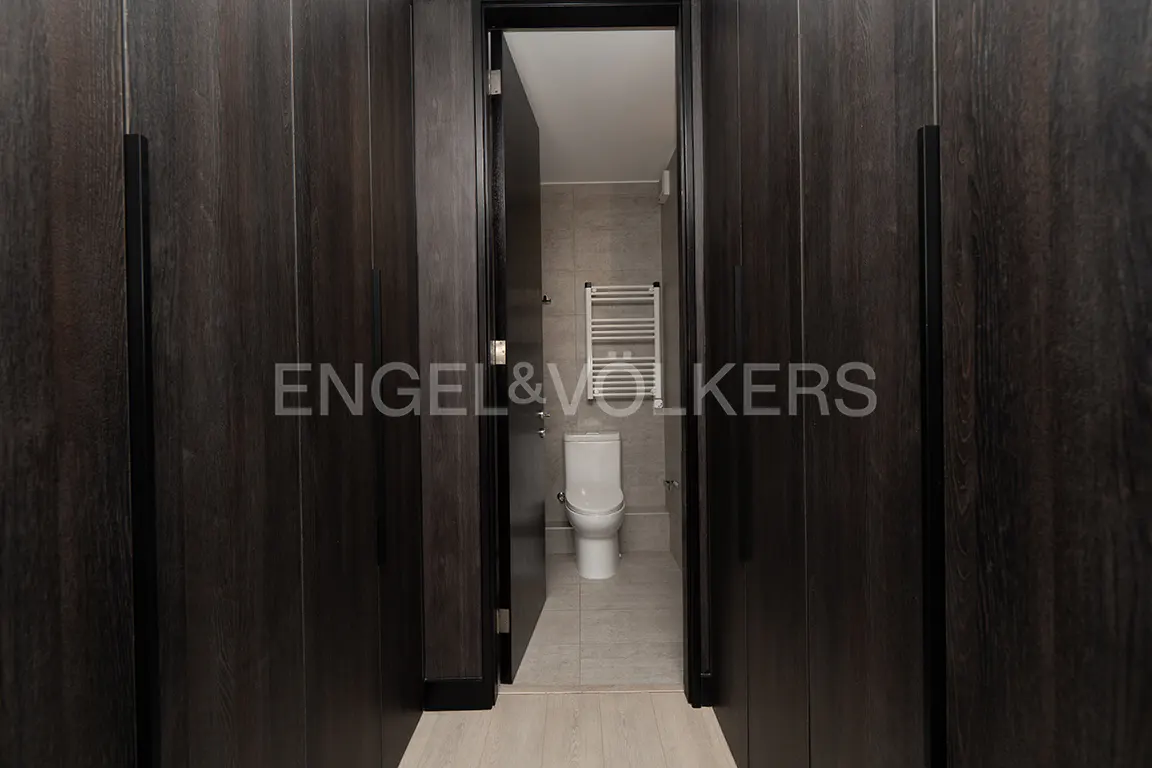 A hallway with dark wood cabinets leads to a bathroom with a toilet and towel rack.