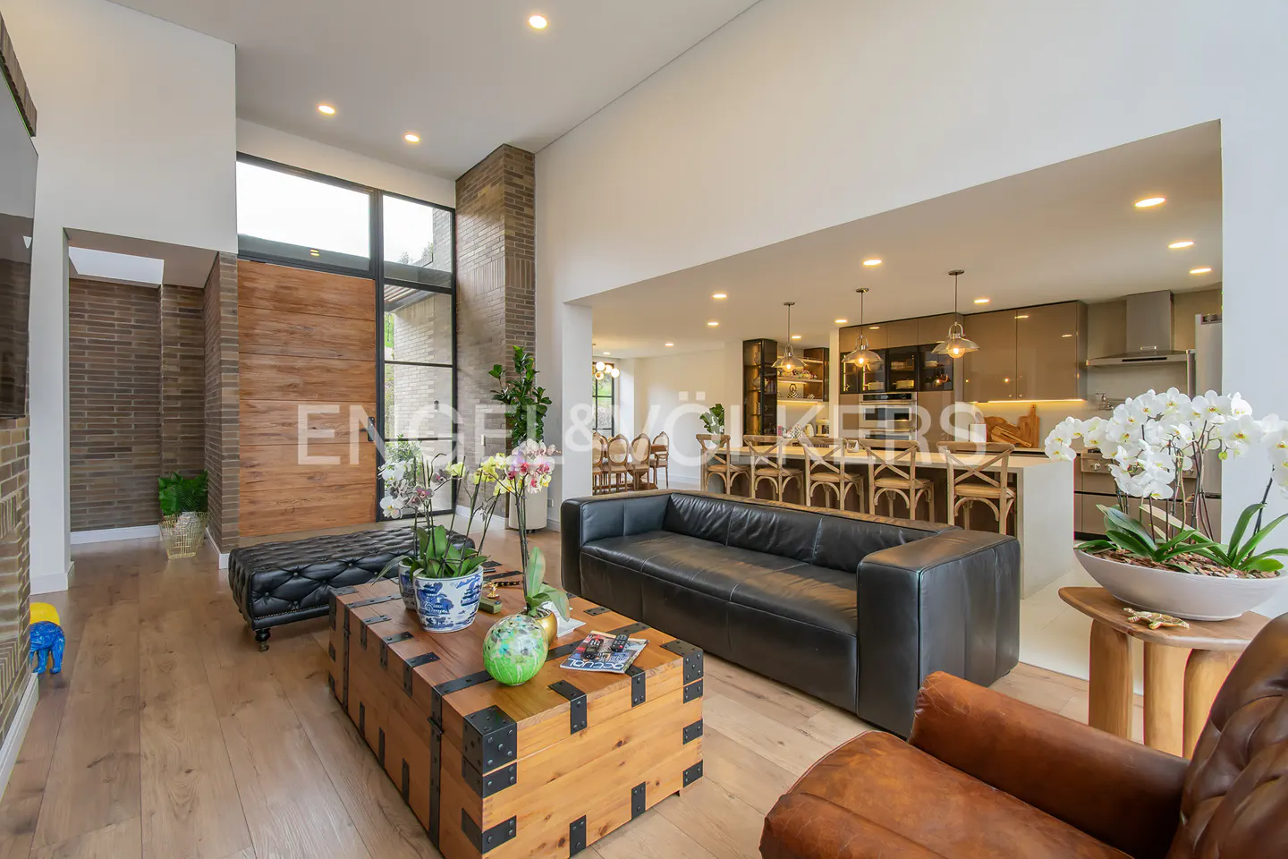 Open-concept living room with a black leather sofa, wooden chest coffee table, and a view into the kitchen with island seating.