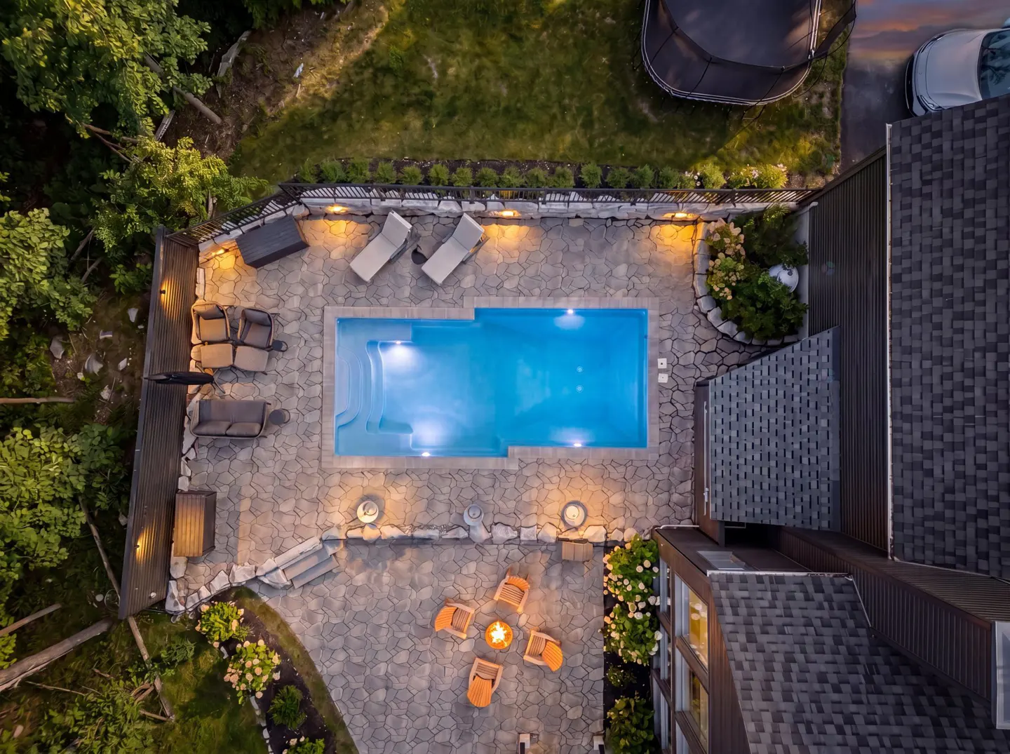 Aerial view of a backyard with a pool, lounge chairs, and a fire pit with orange chairs.