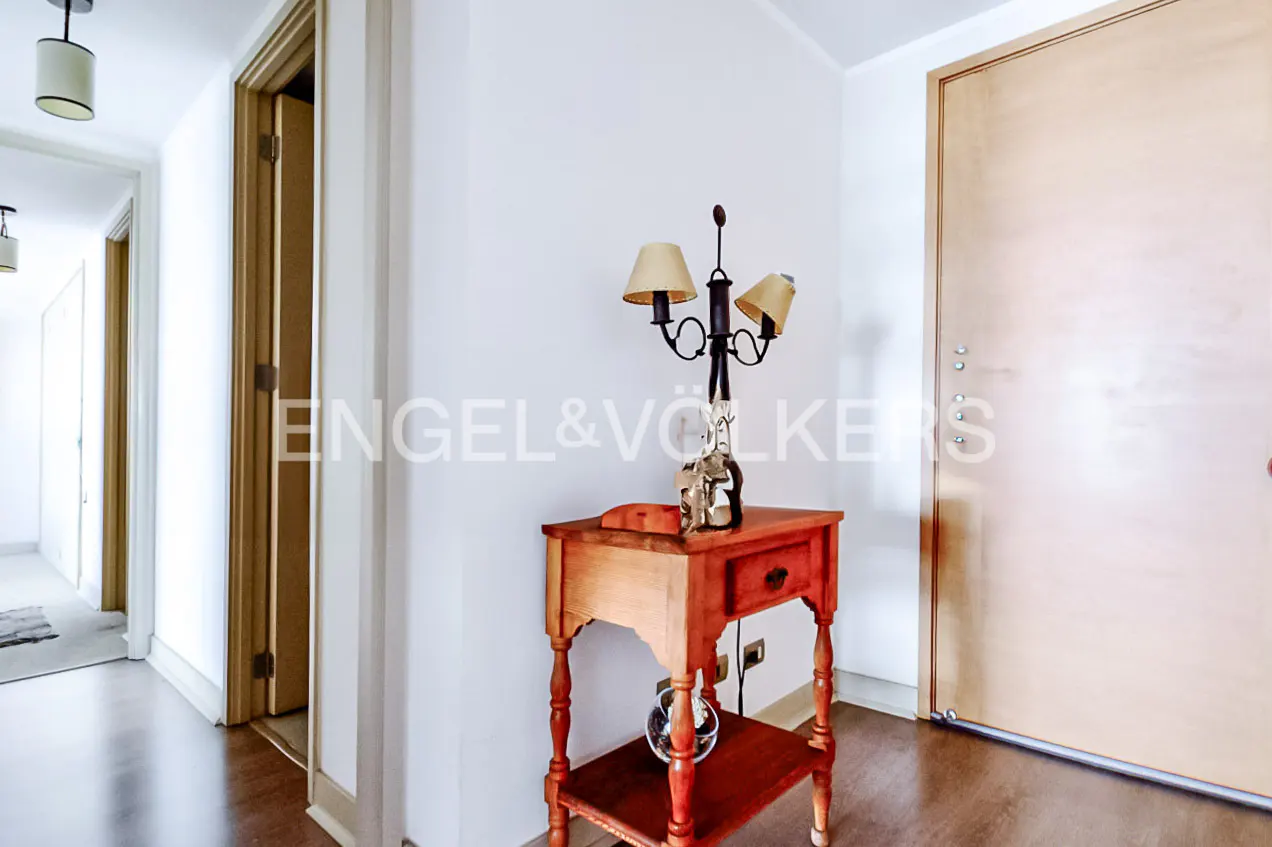 Entryway with a wooden side table, lamp, and decorative items. A light wood door is on the right, and a hallway is on the left.