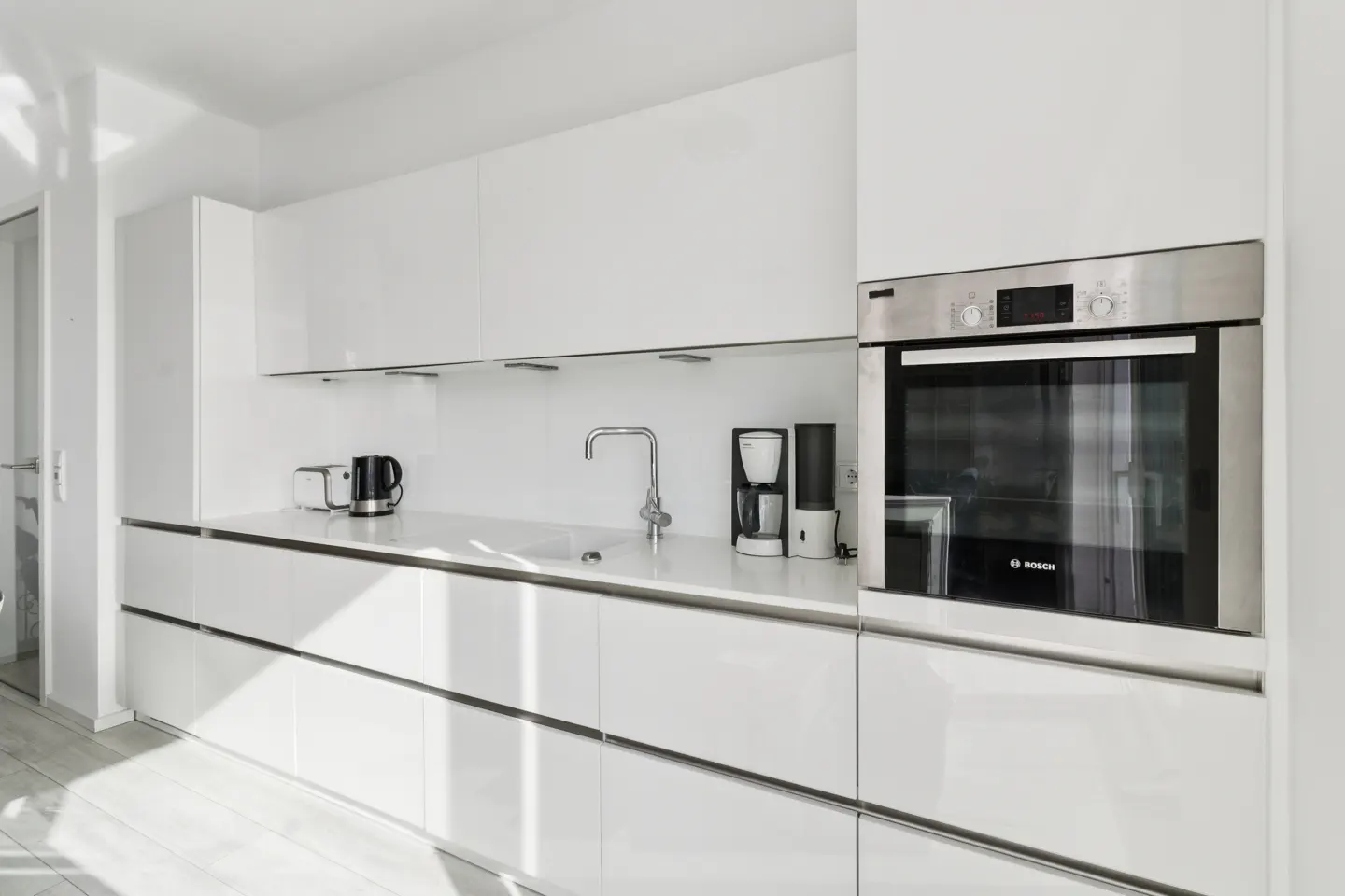 Bright, modern kitchen with white cabinets, stainless steel oven, and appliances. Sunlight streams in from a window.
