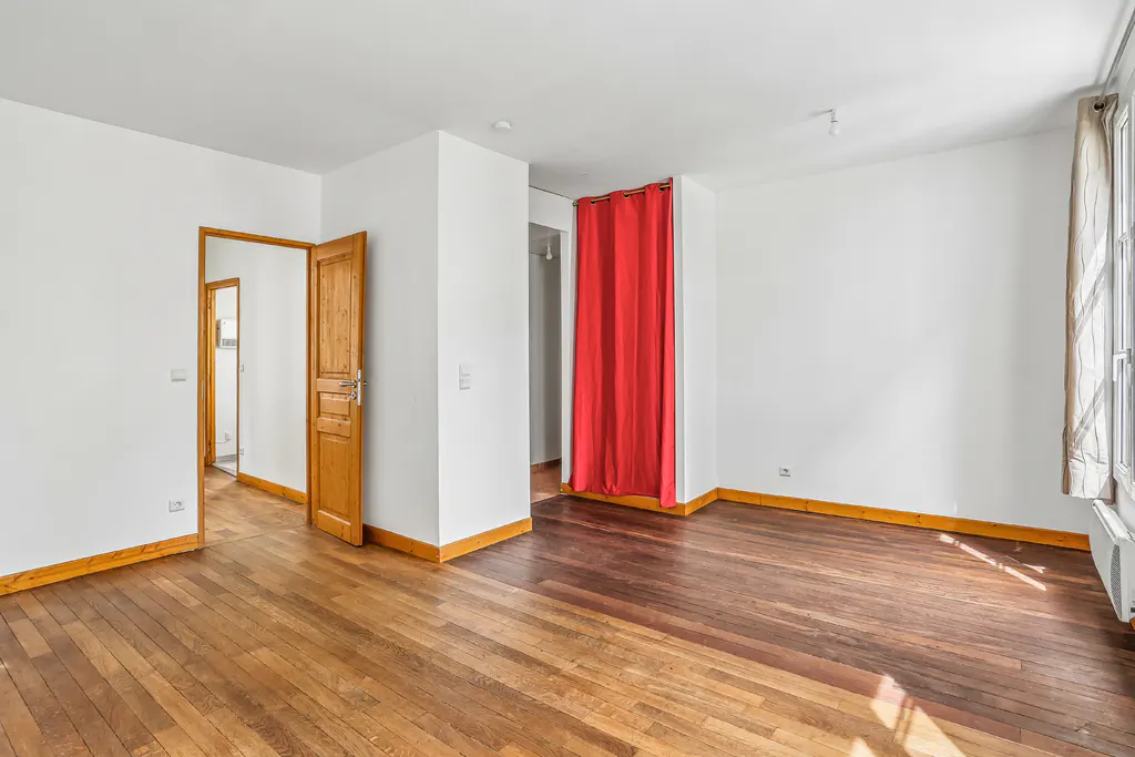 Bright, empty room with hardwood floors, white walls, and wood trim. A red curtain hangs in one doorway, and another door is open.