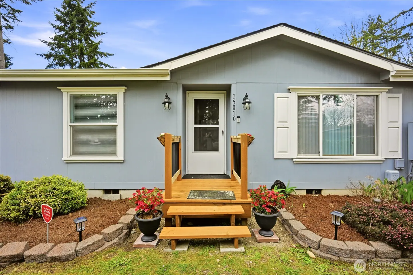 A light blue house with a white door and trim. A small wooden porch with steps leads to the entrance. Flower pots flank the steps.