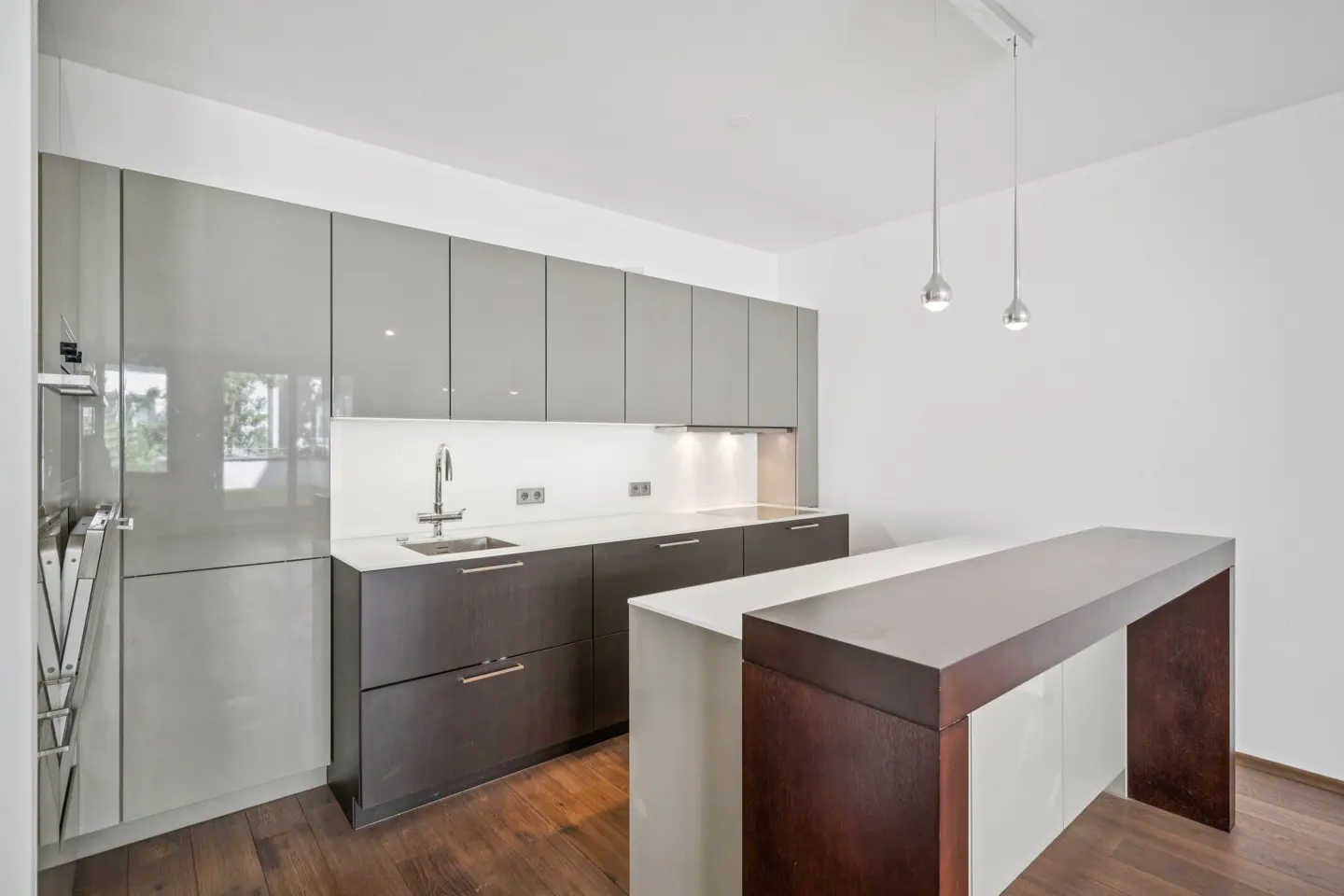 Modern kitchen with glossy grey cabinets, dark wood island, white countertops, and two pendant lights over hardwood floors.