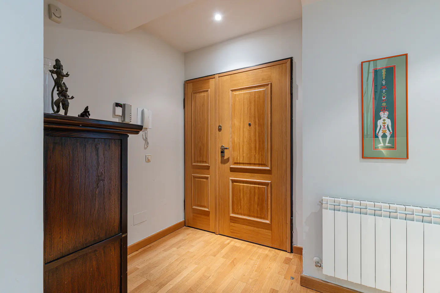 Entryway with light wood floors, double wooden doors, a dark wood cabinet, and a framed colorful artwork on the wall.