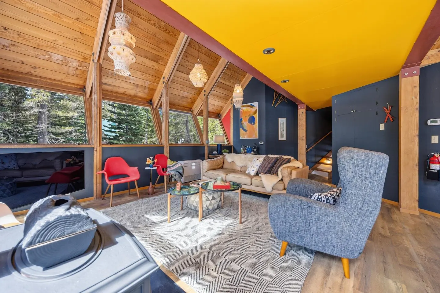 A-frame living room with wood ceiling, yellow ceiling, blue walls, sofa, chairs, and a view of trees.