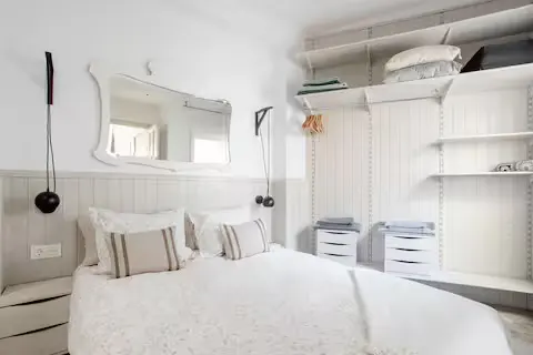 A bright, all-white bedroom with a bed, mirror, and open closet.