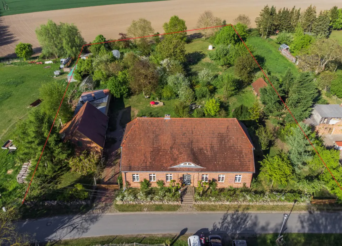 Aerial view of a brick house with a red tile roof, surrounded by trees and a red property line.