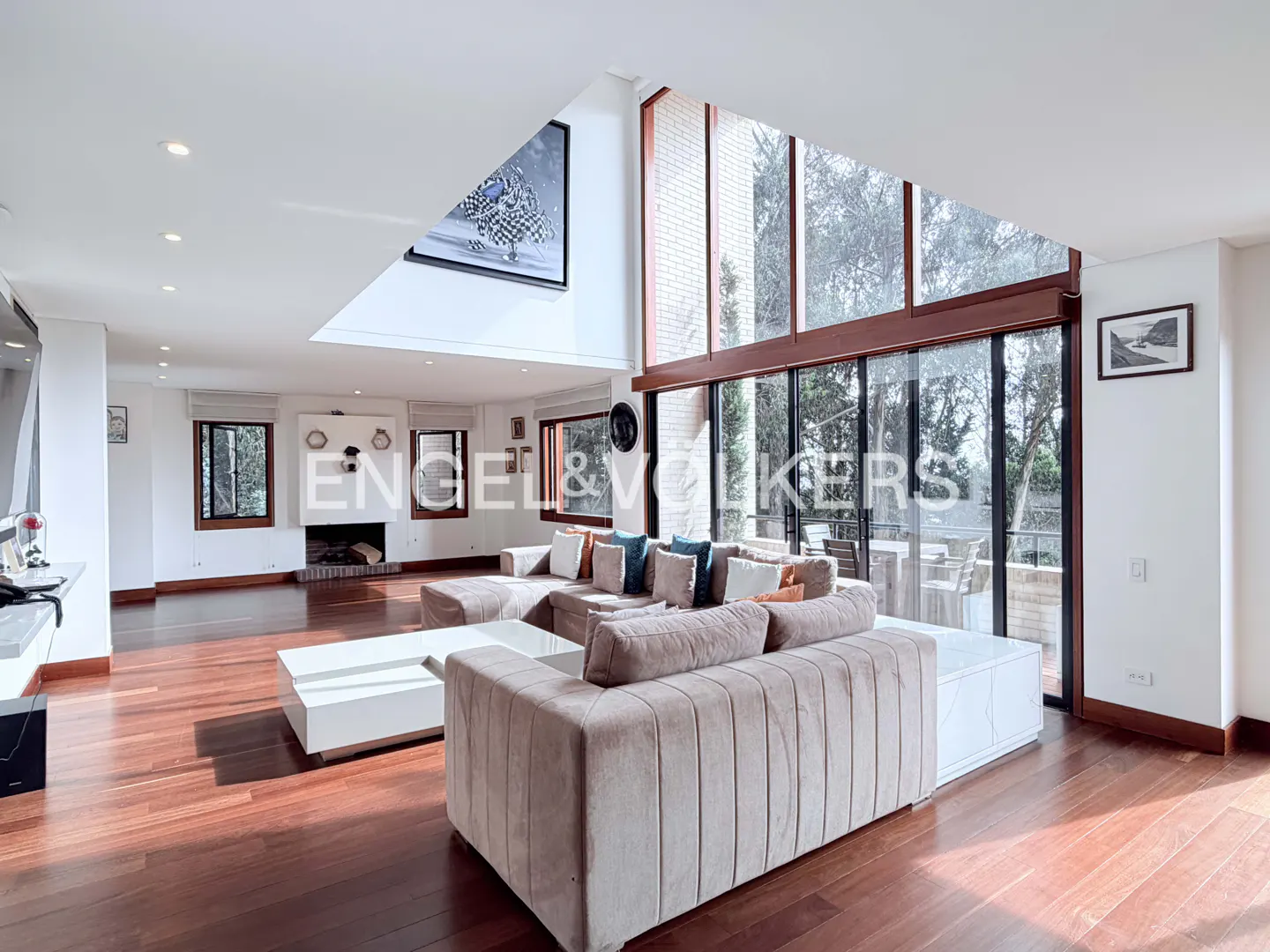 Spacious living room with a beige sectional sofa, white coffee table, hardwood floors, and floor-to-ceiling windows.