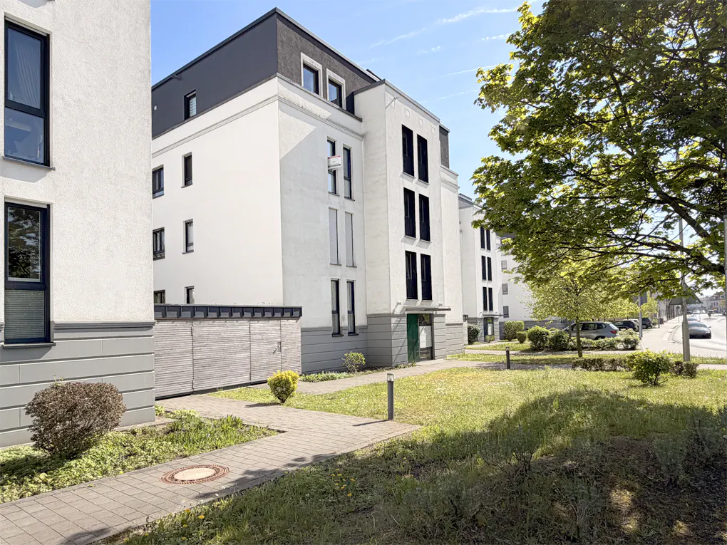 Exterior view of modern white apartment buildings with black trim, green lawn, and a paved walkway.