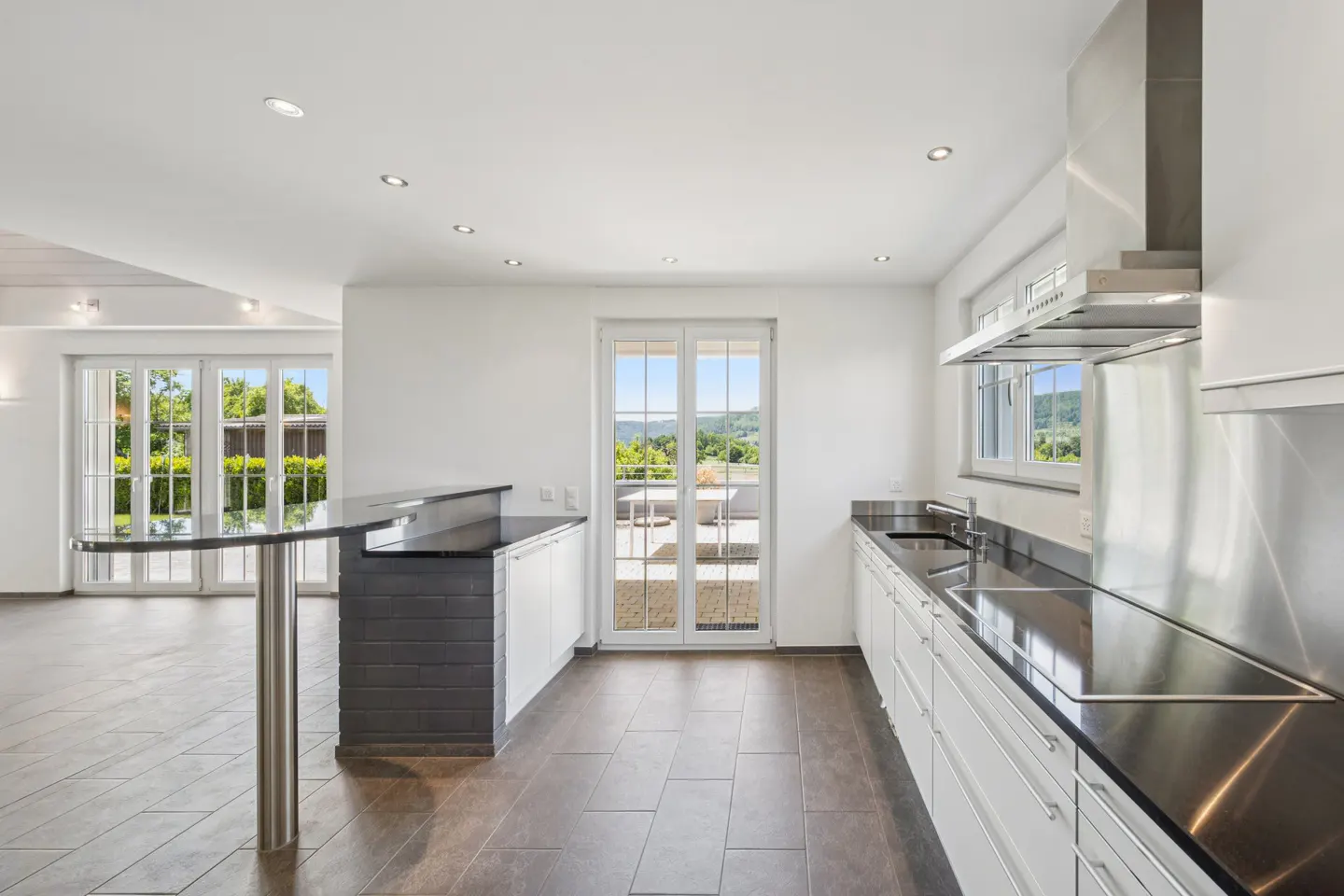Bright, modern kitchen with white cabinets, black countertops, and stainless steel appliances. A bar area and patio doors offer outdoor views.