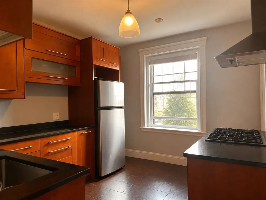 A kitchen with wood cabinets, black countertops, and stainless steel appliances. A window provides natural light.