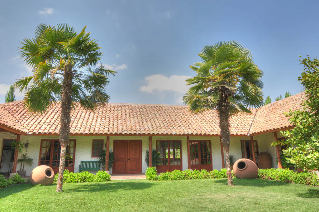 Exterior of a white house with a red tile roof, green lawn, and two palm trees in the front yard.