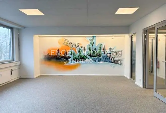 Empty office space with gray carpet and a mural of the city skyline with the Engel & Völkers logo on the wall.