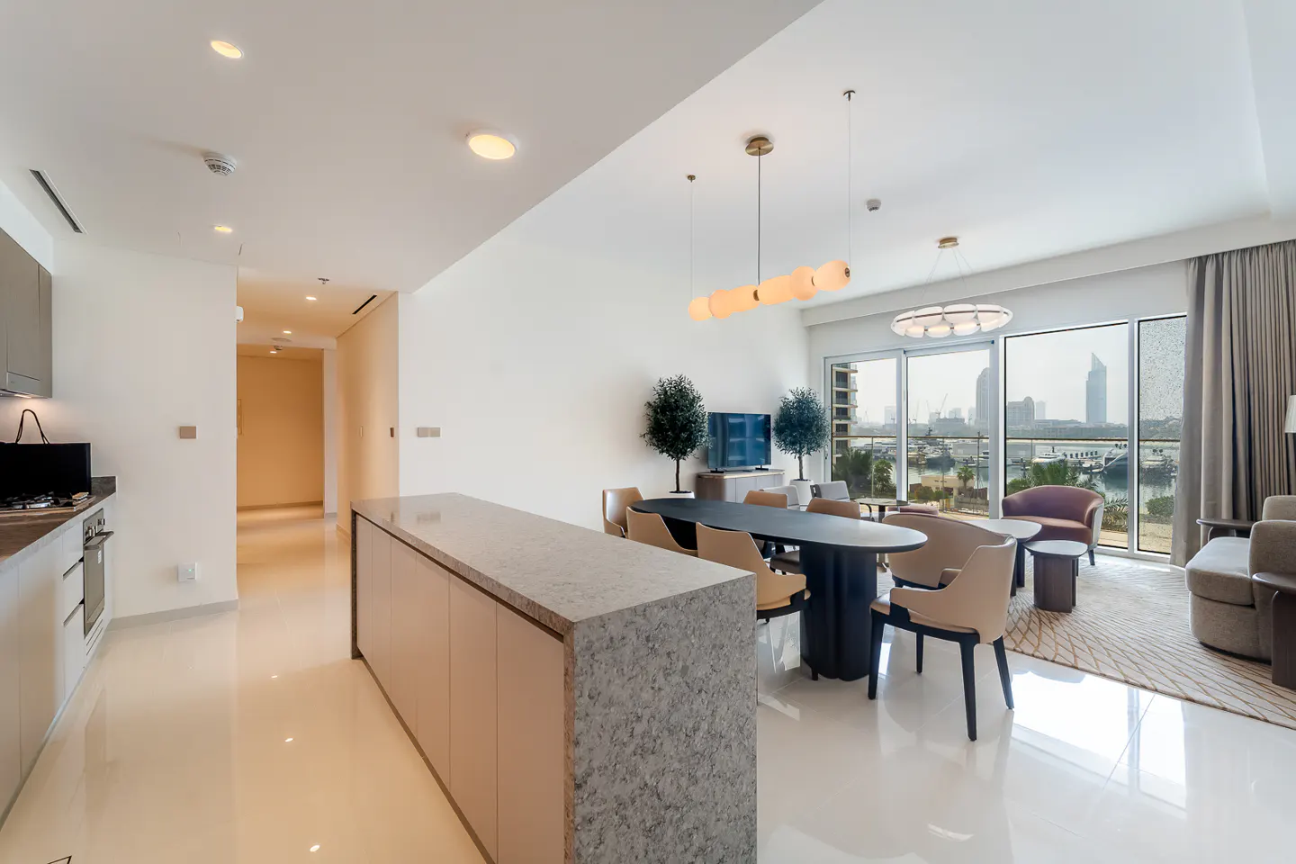 Bright, modern apartment interior with a kitchen island, dining table, and living area overlooking a city and harbor view.