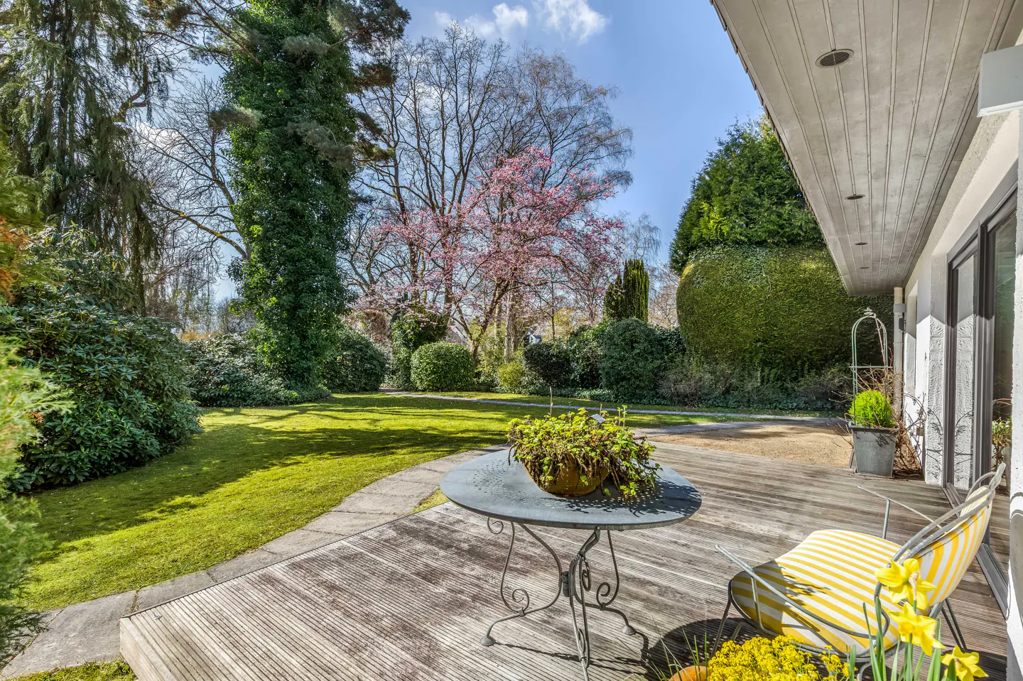 A backyard patio with a table, chairs, and a view of a green lawn and trees.
