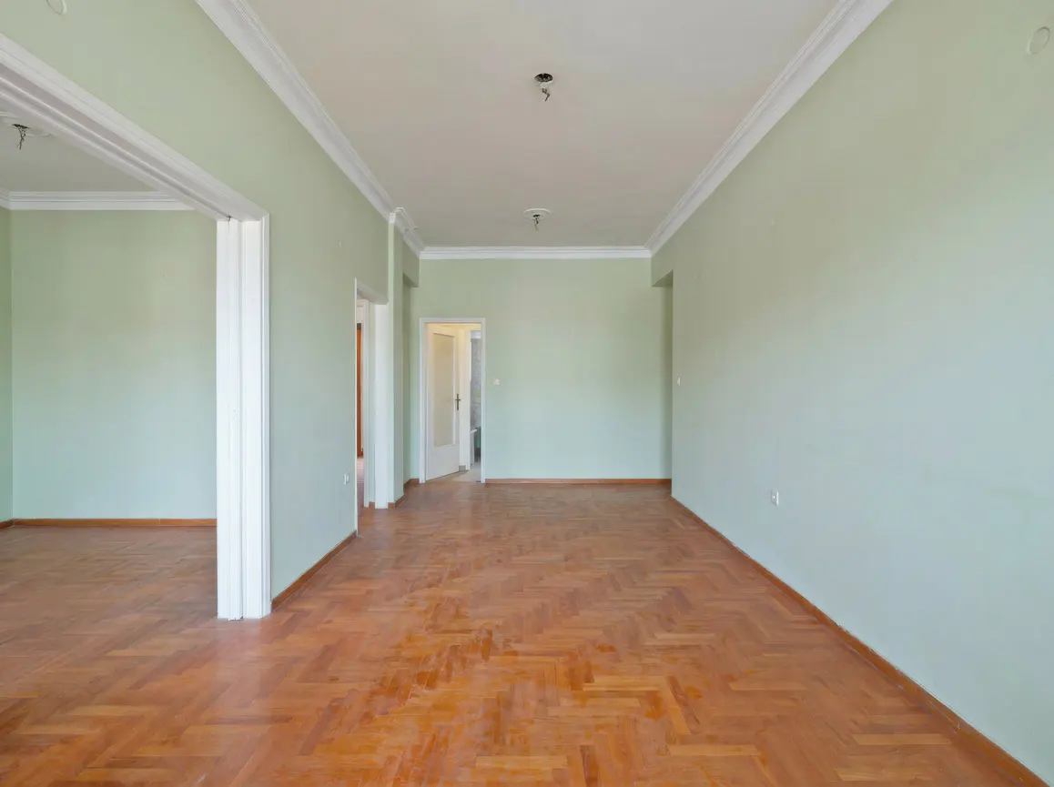 Empty room with light green walls, white trim, and herringbone wood floors. Open doorways lead to other rooms.