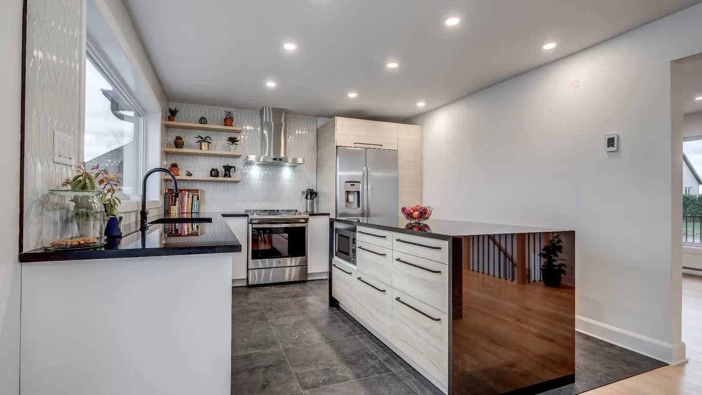 Bright, modern kitchen with white cabinets, black countertops, stainless steel appliances, and a wood-paneled island. Shelves hold plants.