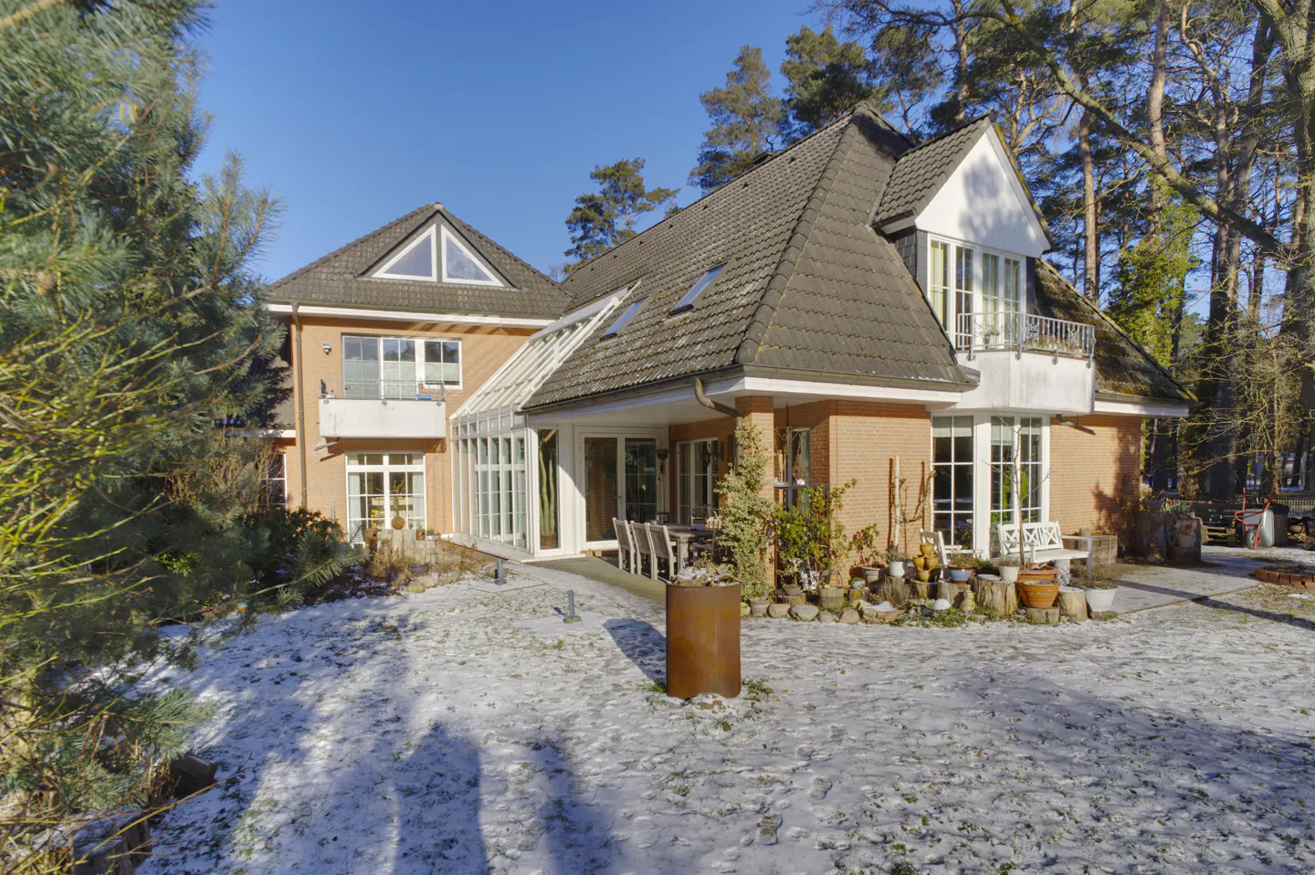 Exterior view of a two-story brick house with a dark roof, white trim, and a sunroom, surrounded by trees and a snowy lawn.
