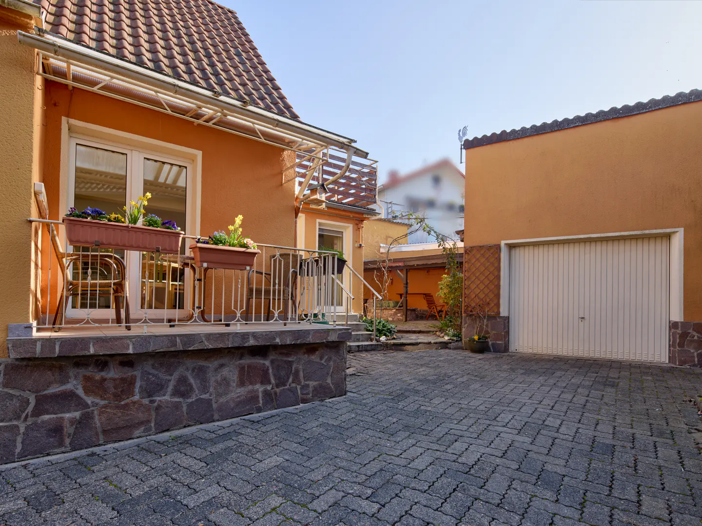Exterior view of an orange house with a stone foundation, a balcony with flower boxes, and a garage with a white door.