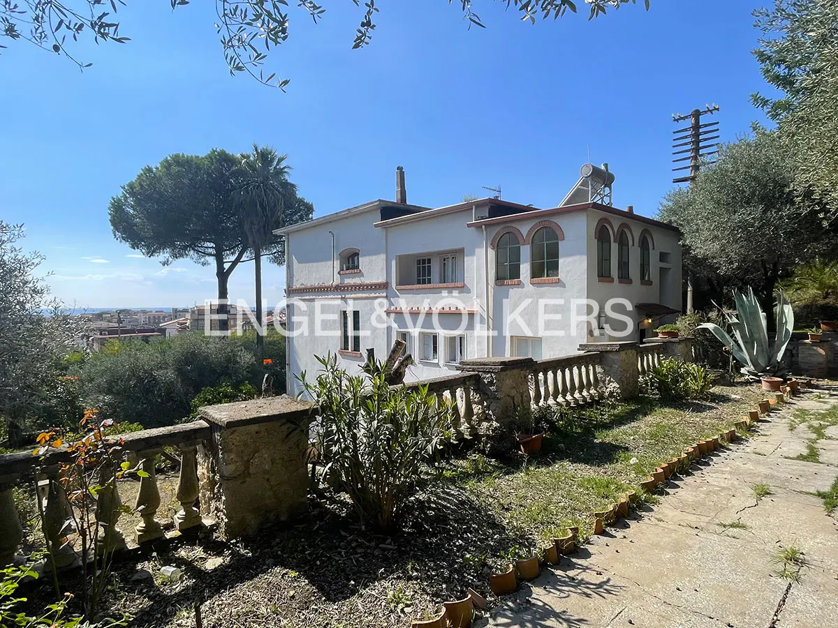 White Mediterranean villa with arched windows, stone balustrade, and garden path under a clear blue sky.