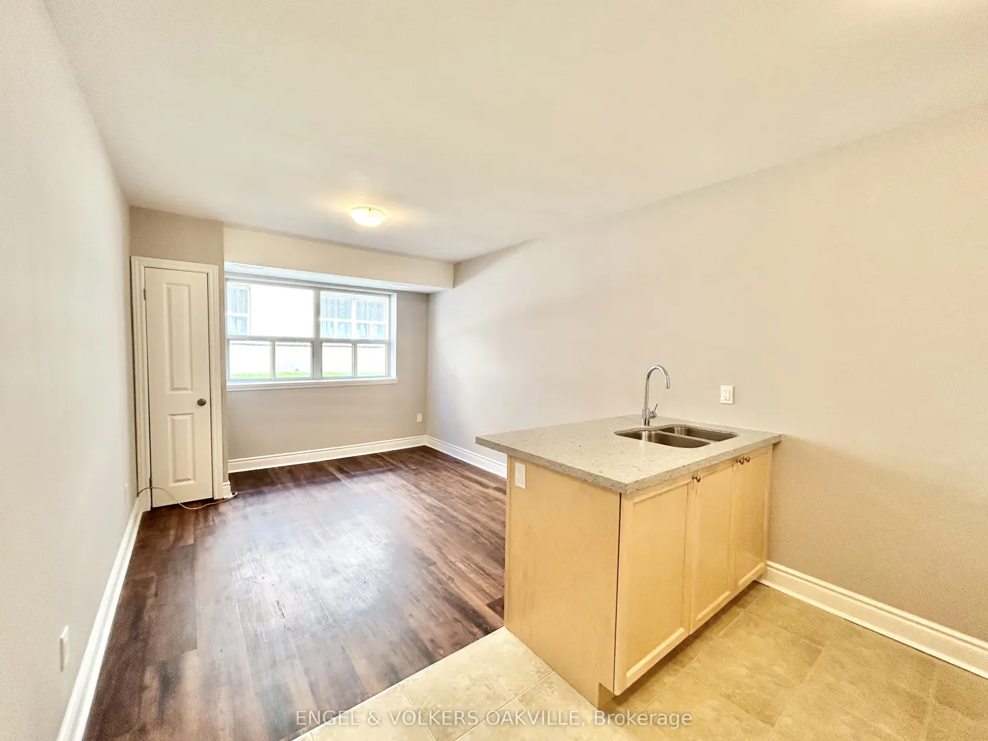 Studio apartment with wood floors, a window, and a small kitchen area with a sink and cabinets.