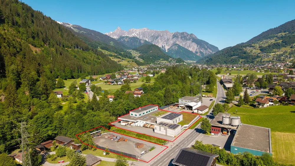 Aerial view of a commercial property outlined in red, set in a lush green valley with snow-capped mountains in the distance.