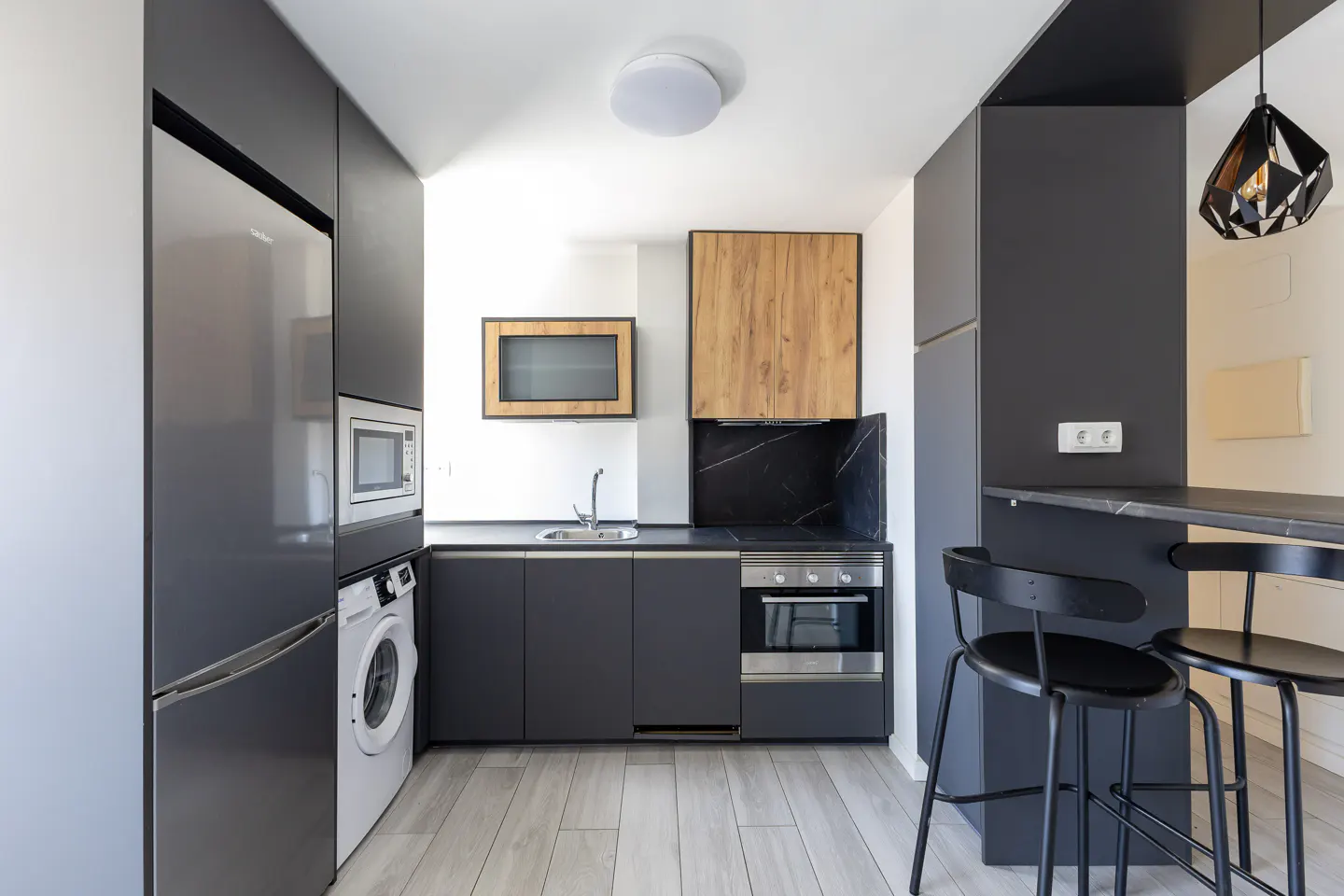 Modern kitchen with gray cabinets, stainless steel appliances, and a black countertop bar with two black stools.