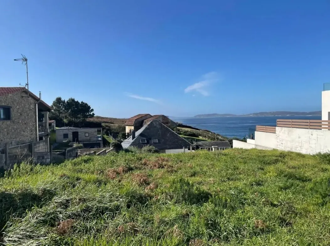 View of a grassy lot with houses, and the ocean in the background under a blue sky.