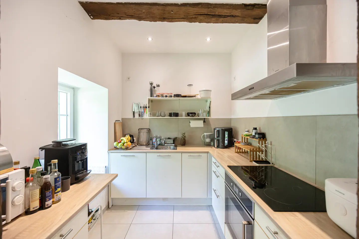 Bright kitchen with white cabinets, light wood countertops, and stainless steel appliances. A wooden beam accents the ceiling.