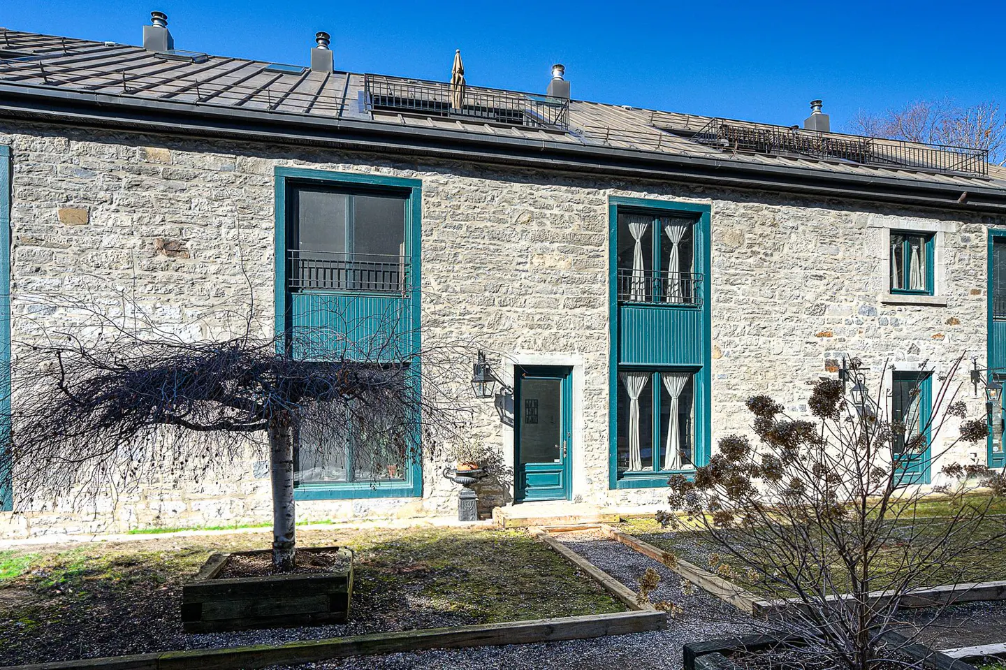 Exterior of a stone building with teal window frames and door, under a blue sky.