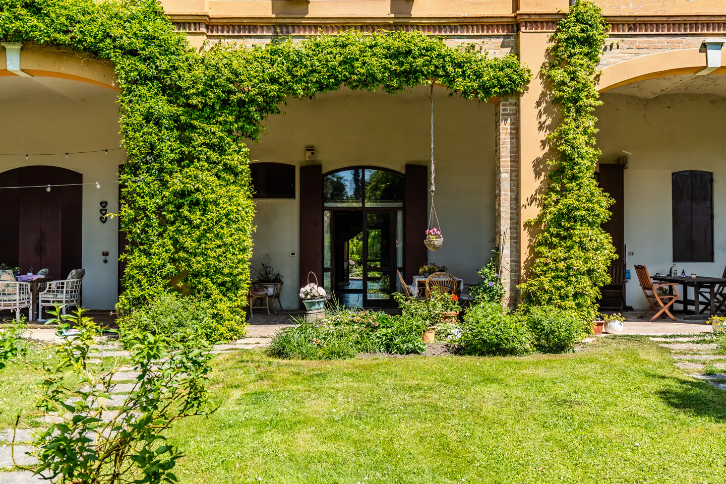 Exterior view of a tan building with green vines covering the columns and archways, with a green lawn in front.