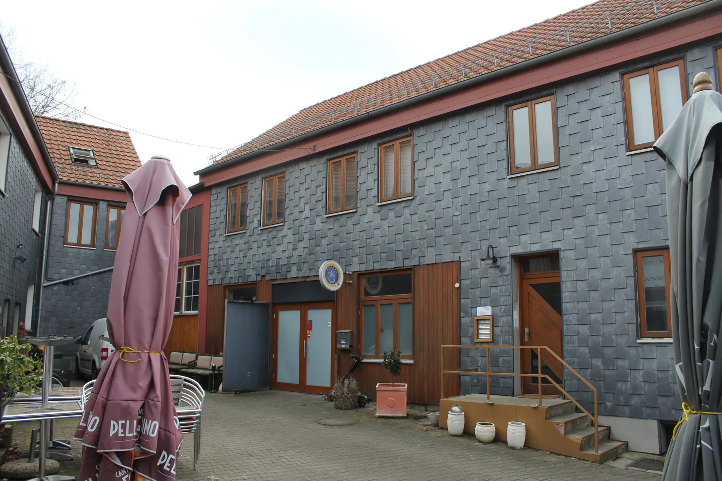 Exterior view of a two-story building with gray shingle siding and brown trim, featuring a central entrance with double doors and a staircase.